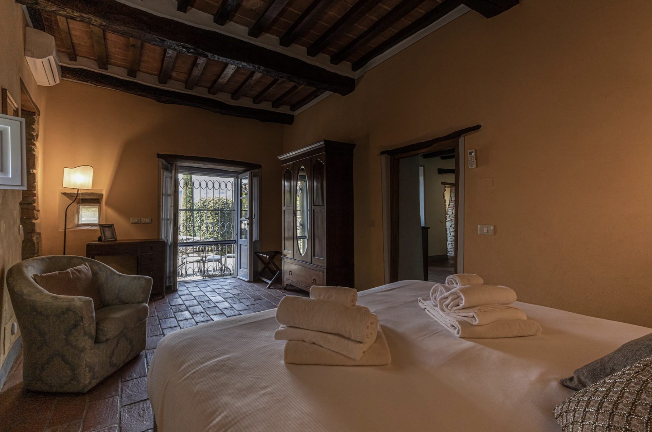 Warm ochre bedroom with beamed ceilings and doors opening to the terrace at Borgo Gaggioleto, Tuscany