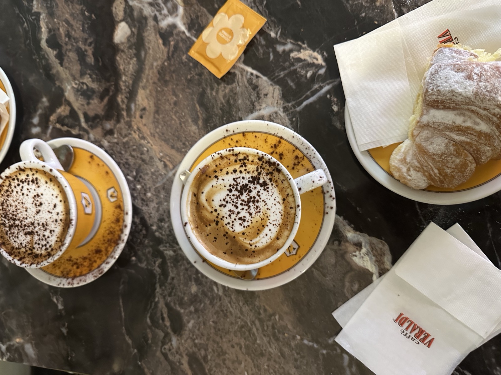 Two cappuccini dusted with cocoa and a cream croissant on the marble counter at our morning bar