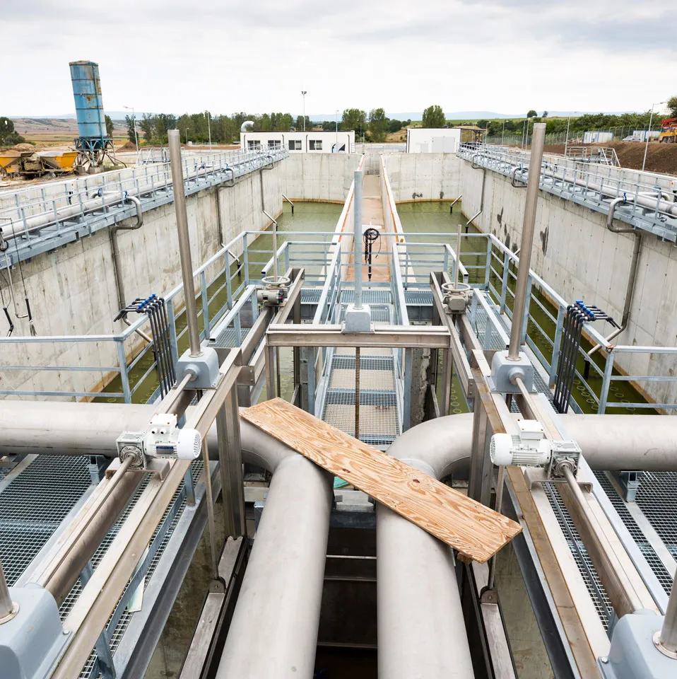 Industrielle Wasseraufbereitungsanlage mit zwei großen Rohren, Metallgeländern und Tanks mit grünlichem Wasser.