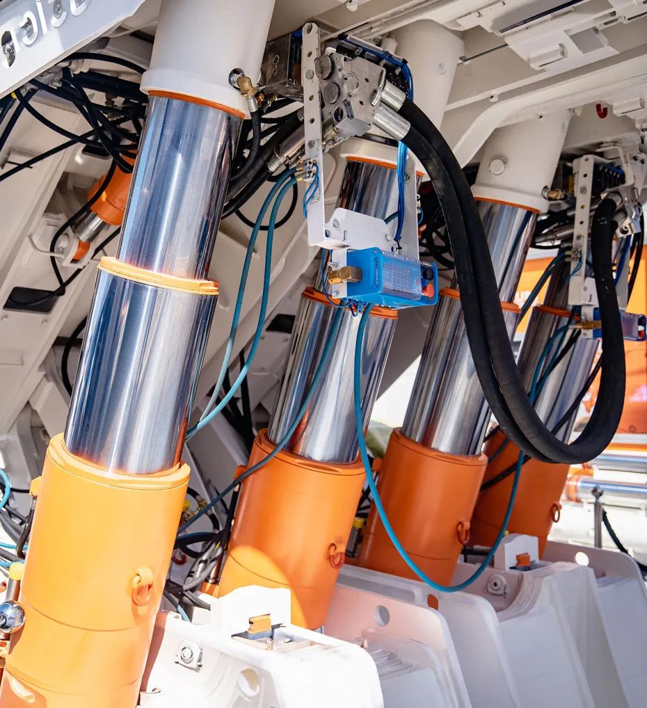 Nahaufnahme von mehreren hydraulischen Zylindern mit orangefarbenen Basen und verbundenen Schläuchen in einem technischen System.