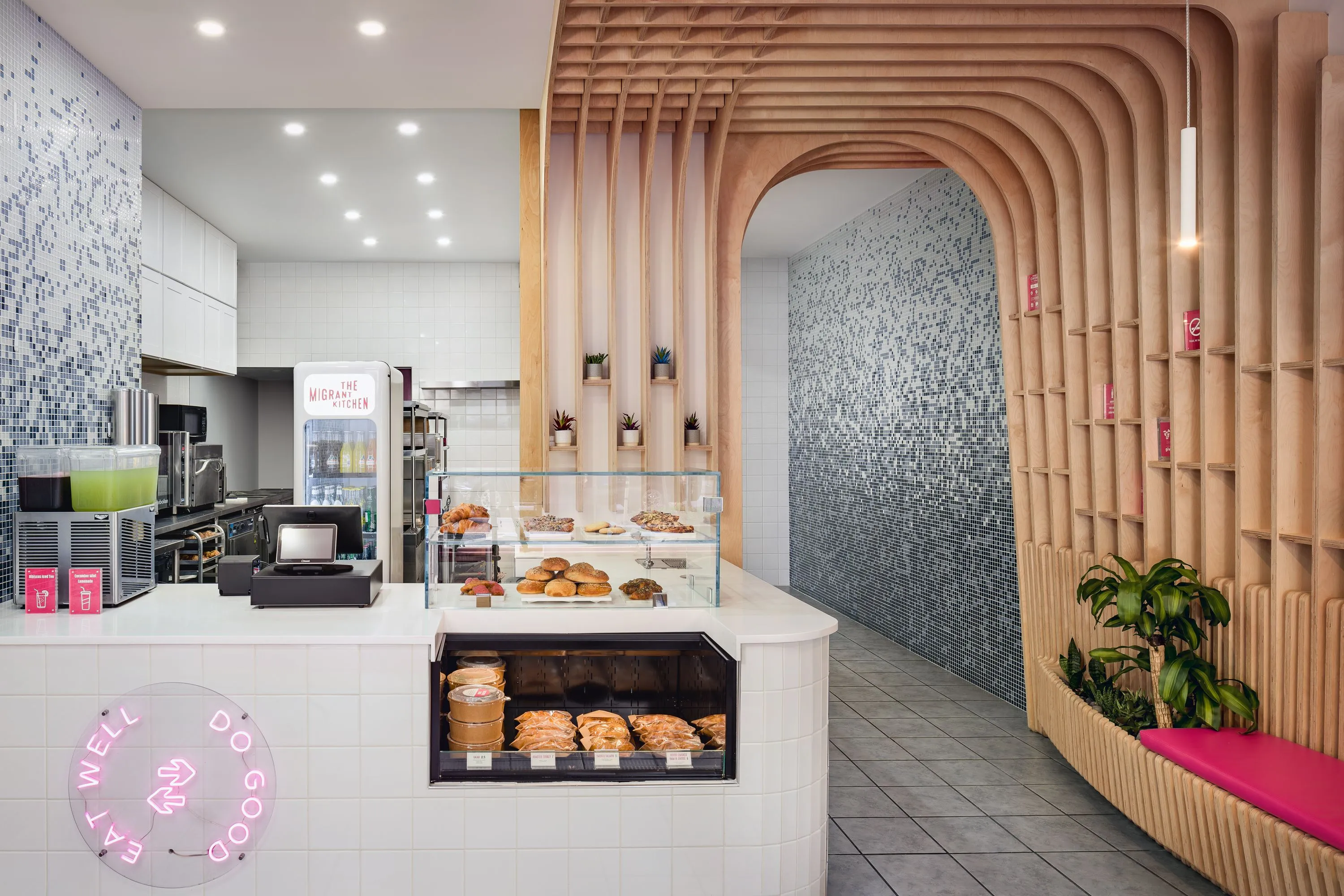 Counter and pastry display beside a birch archway and mosaic wall at The Migrant Kitchen, New York