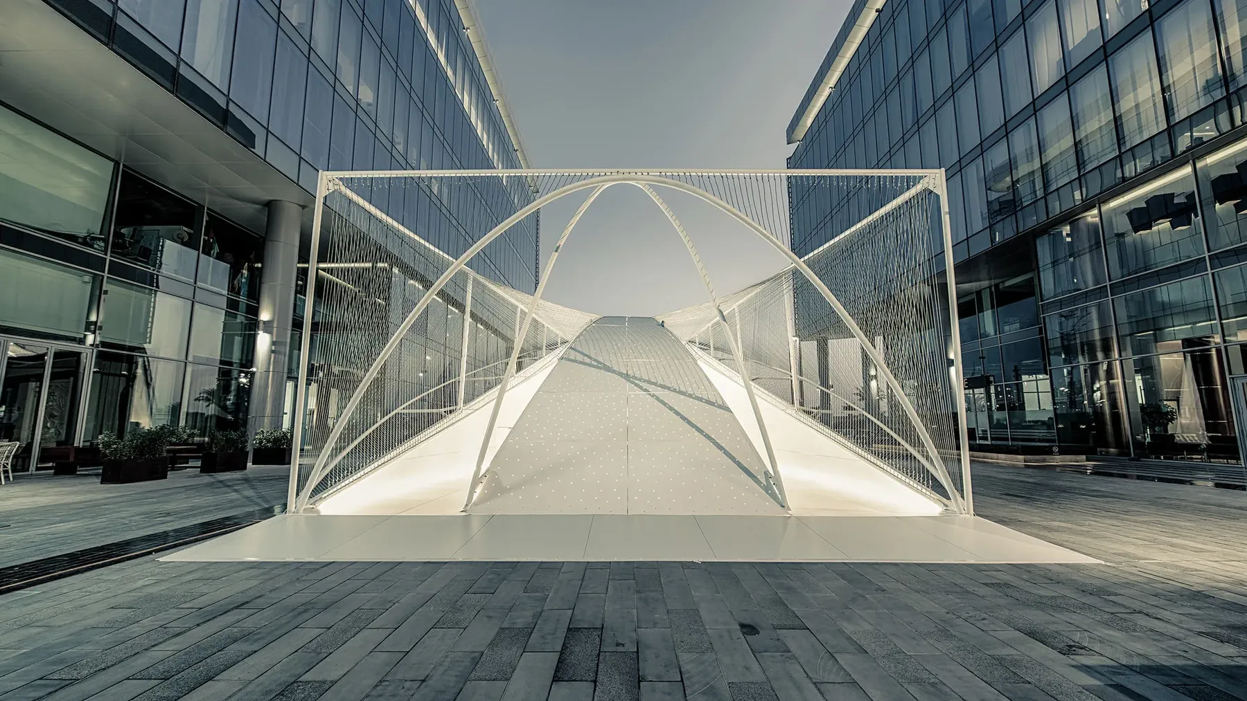 The steel pipe frame of the Audi Innovation Hub seen end on, between two glass buildings.