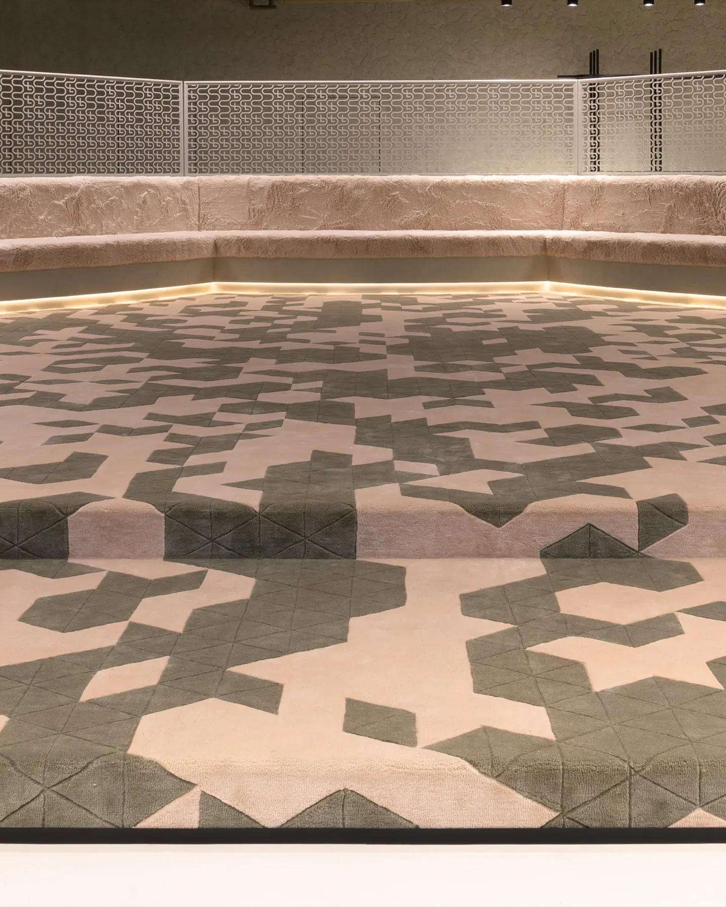 The octagonal seating platform at the center of the Send Location store: a bench around a patterned carpet, a step up to it, a line of light under the seat and a metal mesh screen behind.