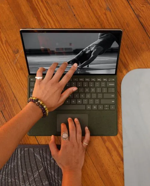 Hands over laptop keyboard watching a black-and-white yoga video on a wooden floor.