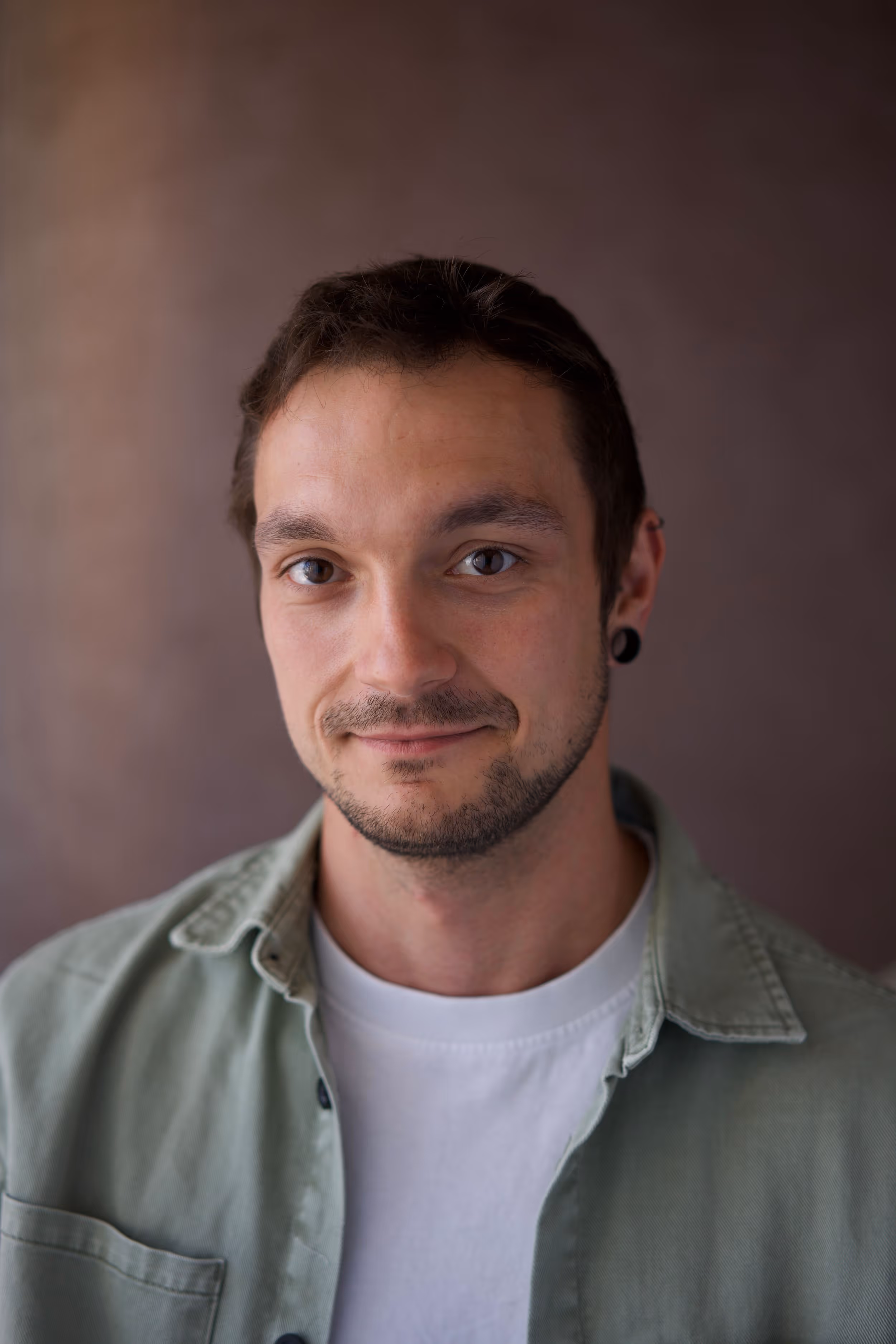 Portrait of a young man with short dark hair, light beard, wearing a green shirt over a white tee.