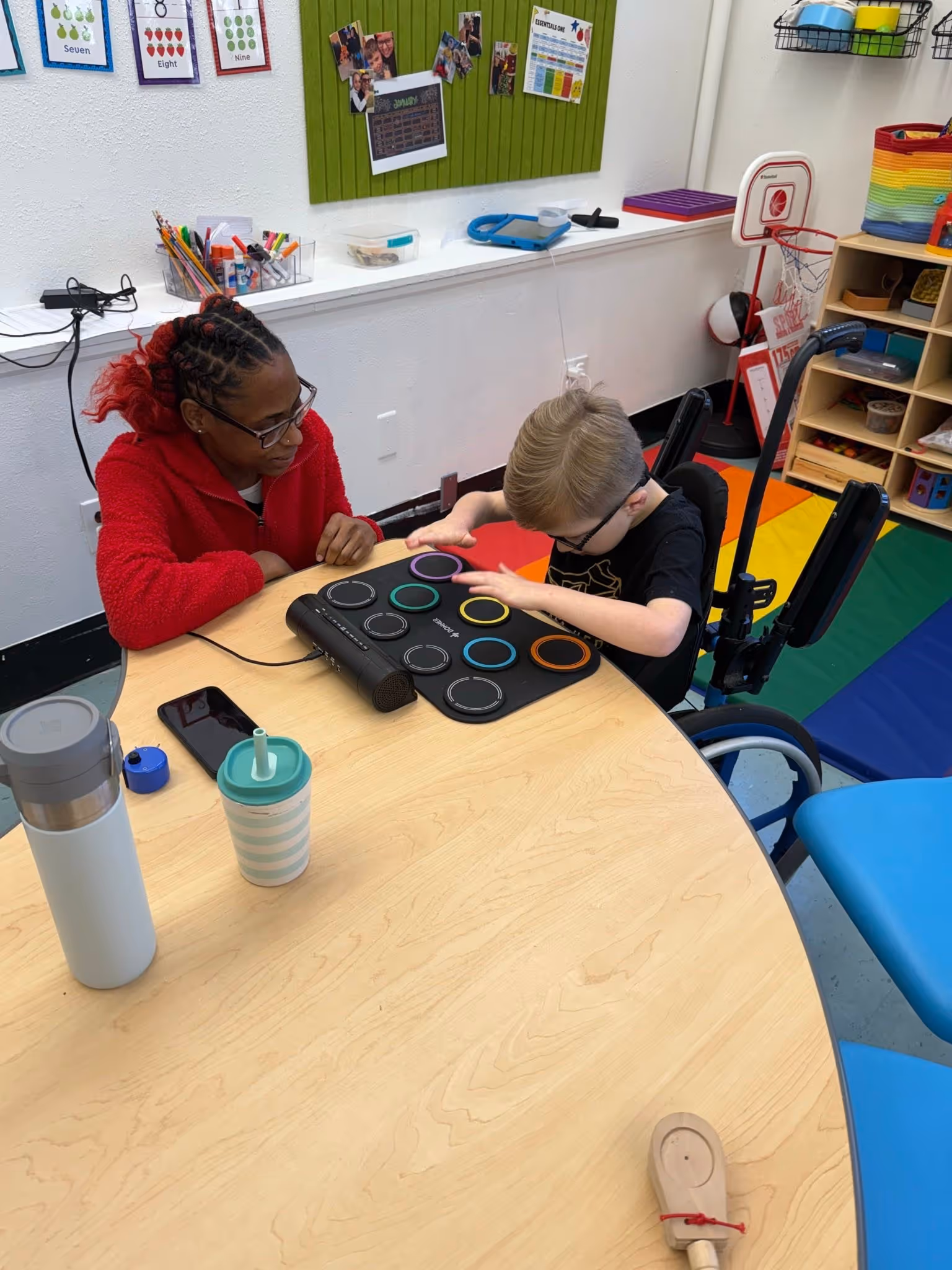 Teacher working one-on-one with a student at a classroom table, guiding them through an interactive activity using a light-up music pad to support focus, coordination, and engagement