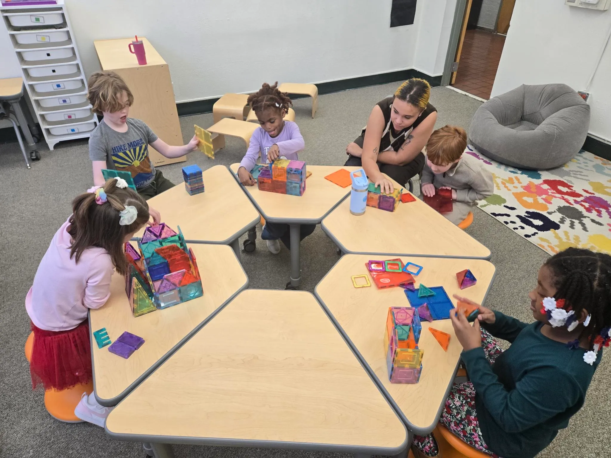 Group of students working together at a classroom table with a teacher, using colorful building tiles to encourage collaboration, creativity, and hands-on learning