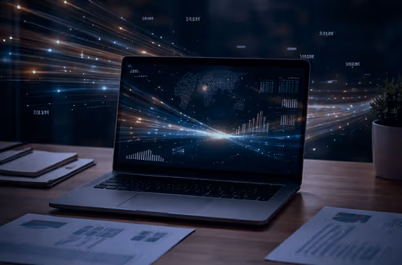 Laptop on a desk displaying data charts and a world map with light streaks representing data flow in the background.