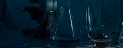 A set of laboratory glassware including beakers and flasks on a dark surface in a dimly lit environment.
