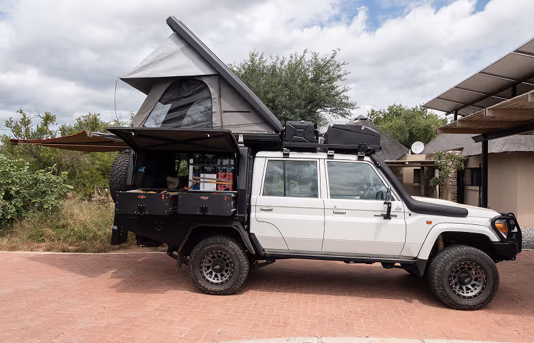 Witte 4x4 terreinauto met uitklapbare daktent en aangepaste achterbak, geparkeerd op een stenen oprit.