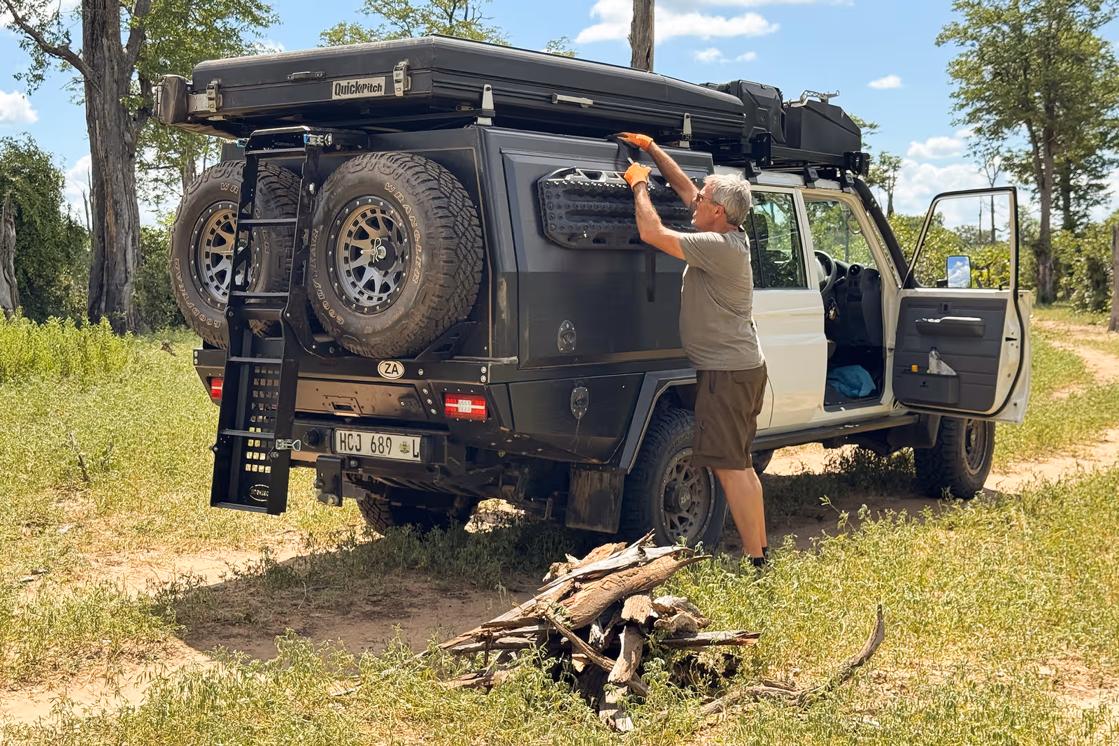 Peter die op een off-road voertuig aan het kampvuur hout vastmaakt in een groene open veldomgeving.