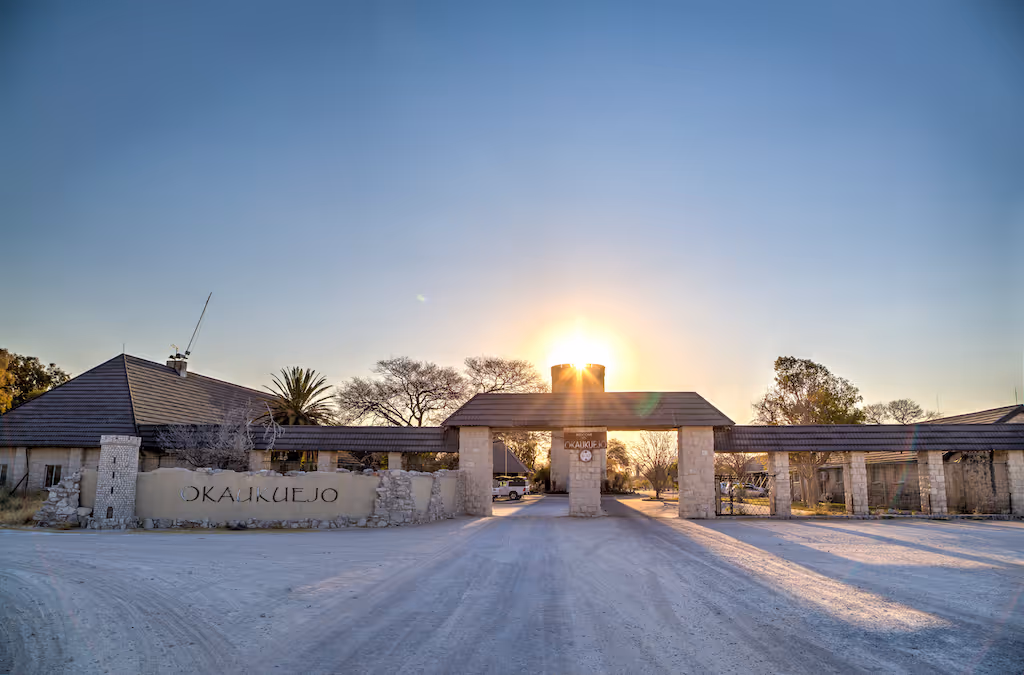 Ingangspoort van Okaukuejo kamp in Namibië bij zonsopgang met zandweg en gebouwen aan weerszijden.