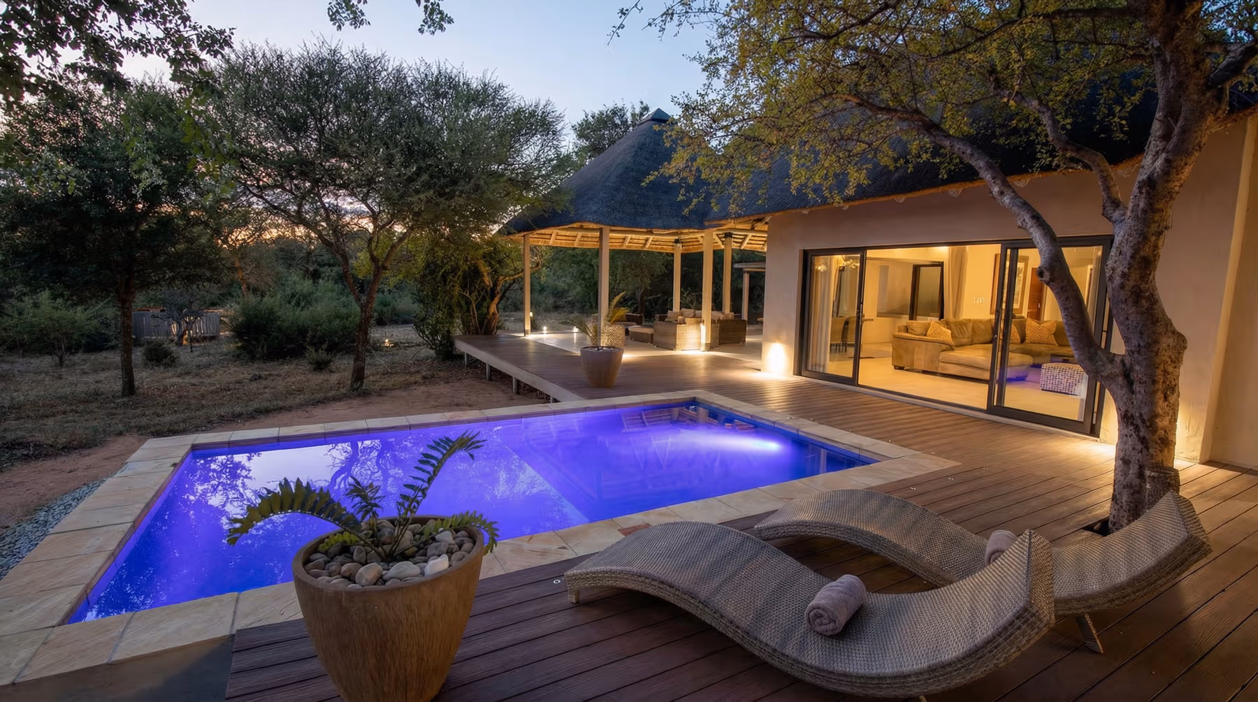 Verlichte zwembad met paarse gloed bij Villa Muningi met loungezetels op het terras en een natuurlijke omgeving bij zonsondergang.