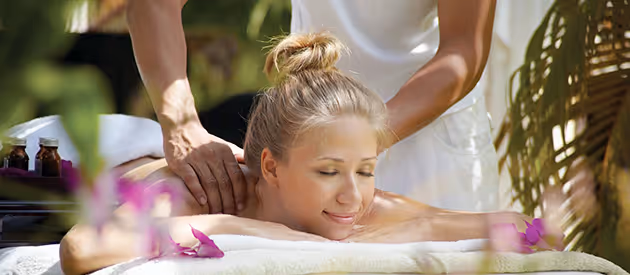 Vrouw die ontspant met gesloten ogen terwijl ze een rugmassage krijgt in een rustige, natuurlijke omgeving.
