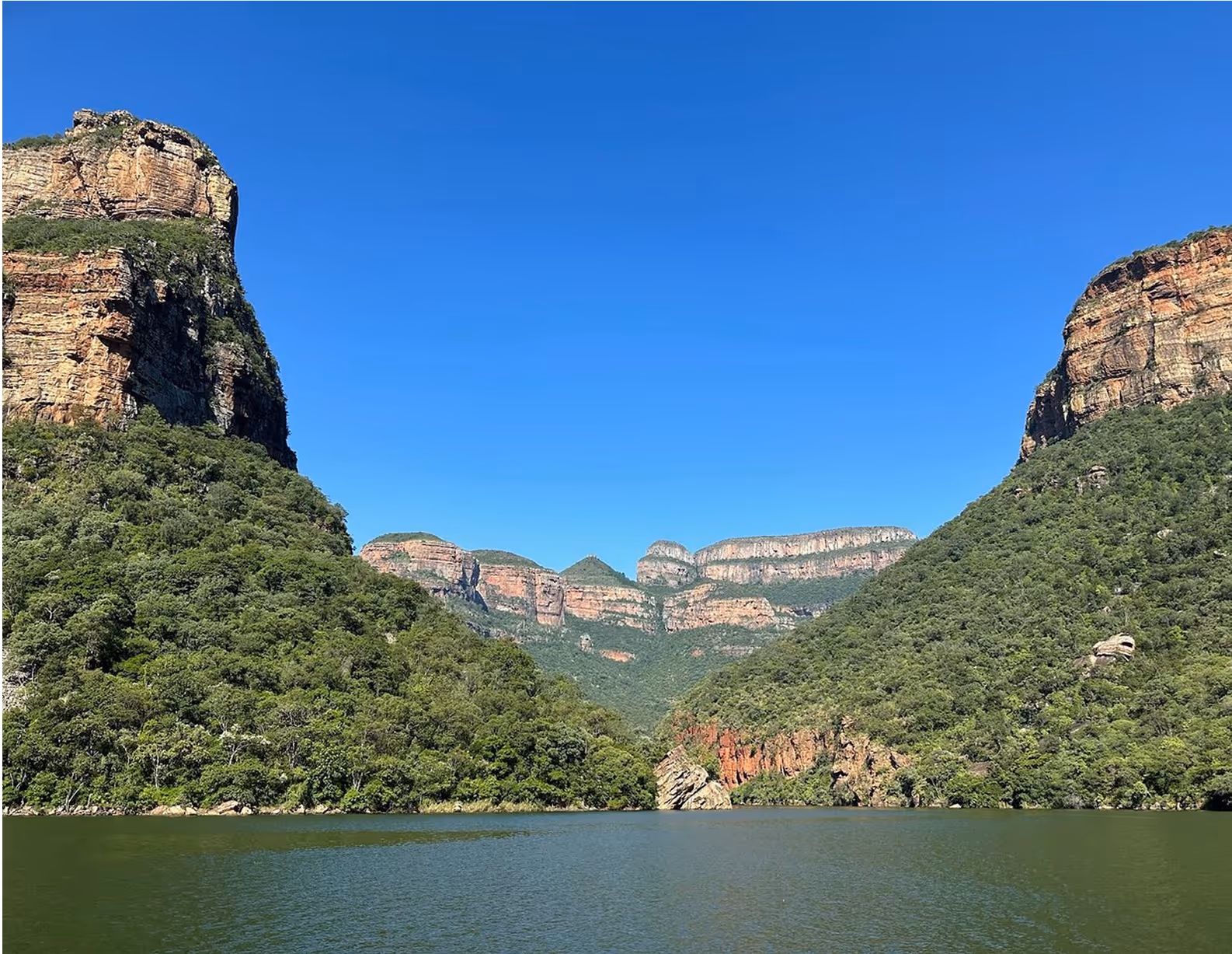 Uitzicht op Blyde River Canyon met groene bossen, rotsformaties en een blauwe lucht boven een rustige rivier.