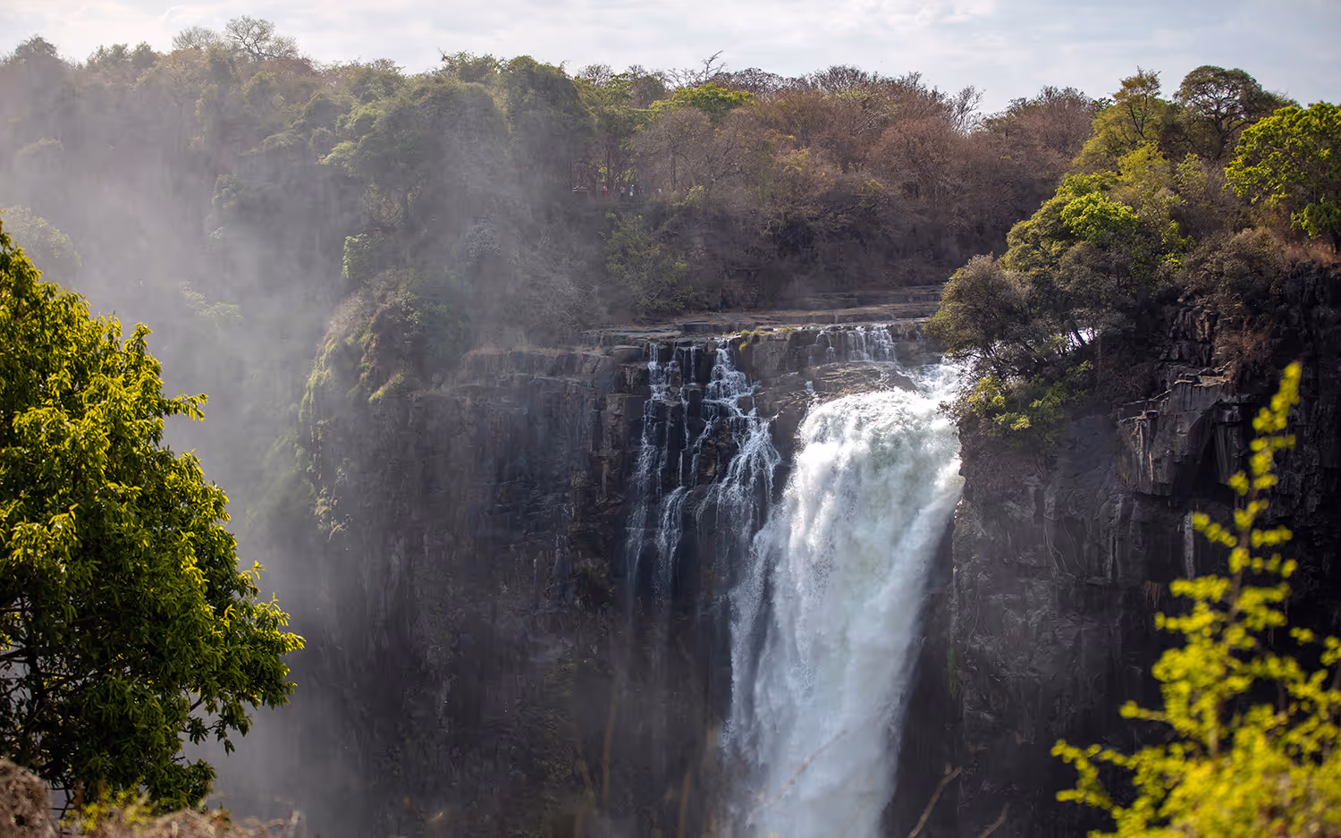 Waterval met nevel en groene bomen rondom een rotsachtige klif.