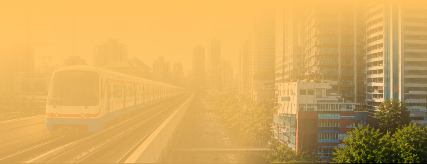 An elevated train moves along a track on the left, with tall buildings and green trees on the right, under a hazy, orange-yellow sky.