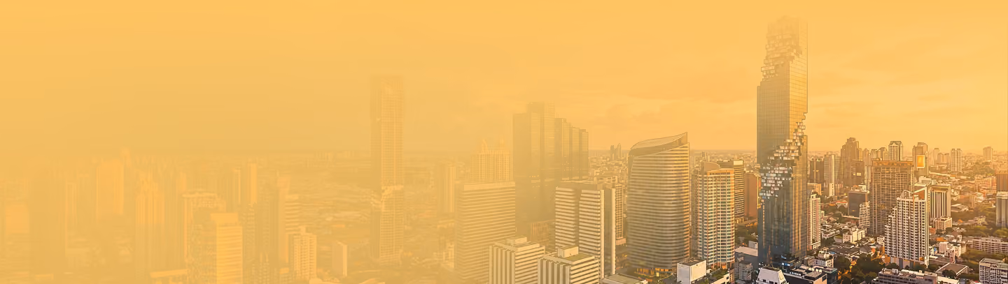 City skyline at sunset with modern skyscrapers, including a tall building under construction covered with cranes.