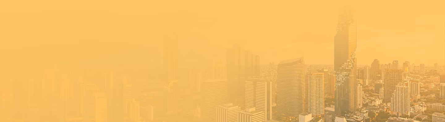 City skyline with tall buildings partly obscured by haze against an orange-tinted sky.