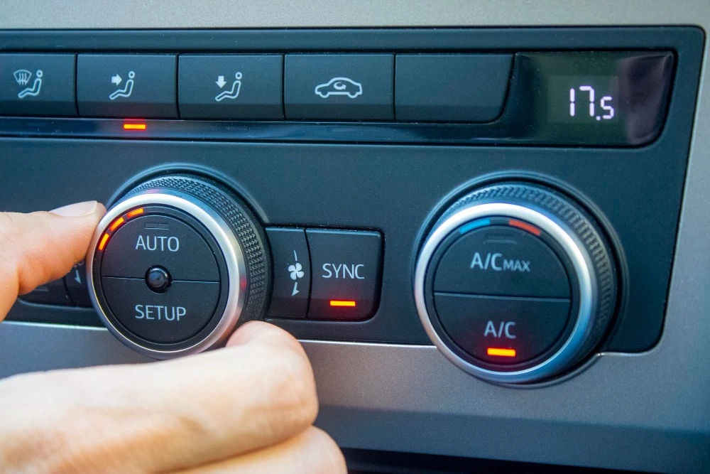 Hand adjusting car climate control knob set to 17.5 degrees with AUTO, SYNC, and A/C buttons.
