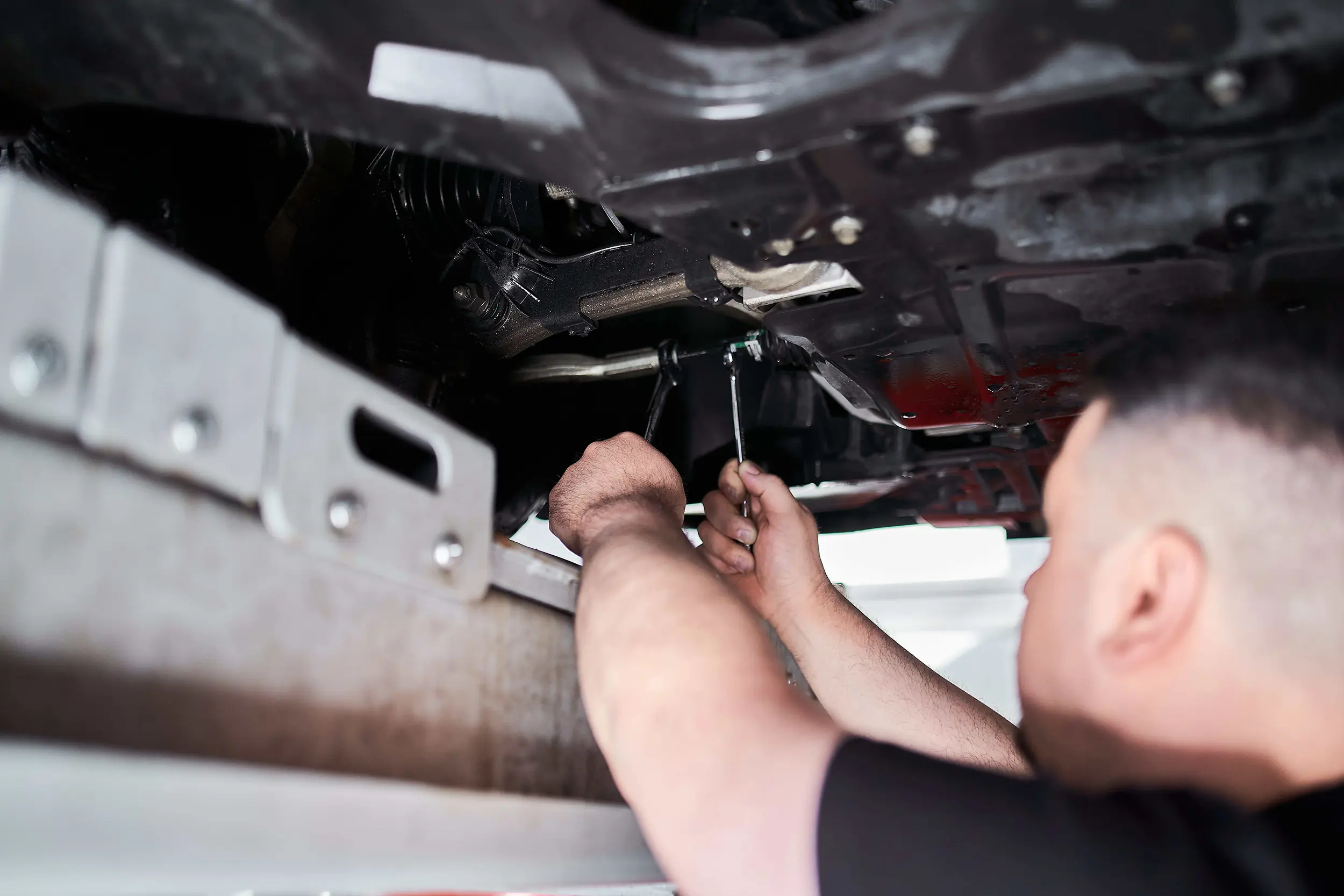 Person using tools to repair or work on the underside of a vehicle in a garage.