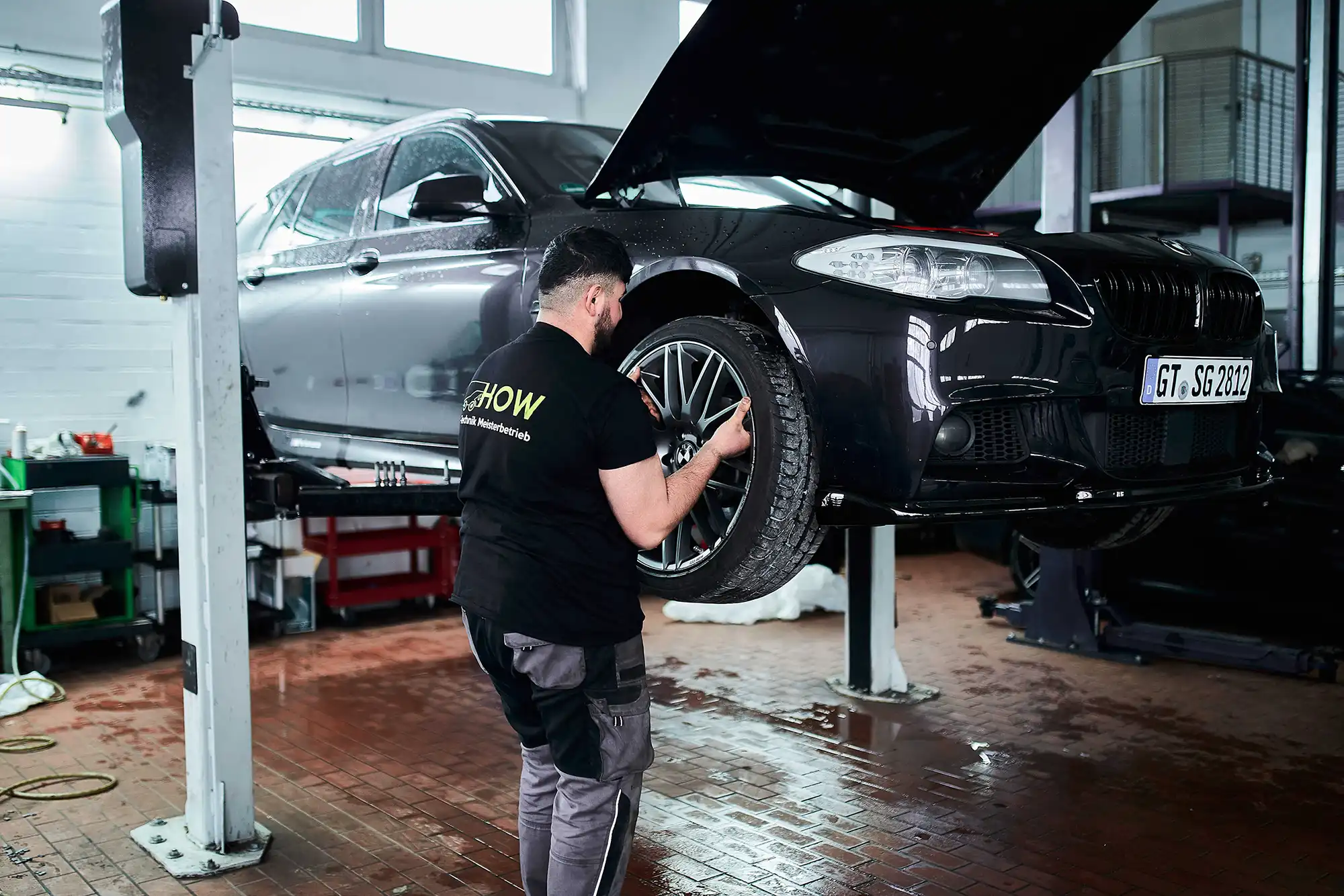 Mechanic working on a car tire with the car lifted inside a garage with tools and equipment.