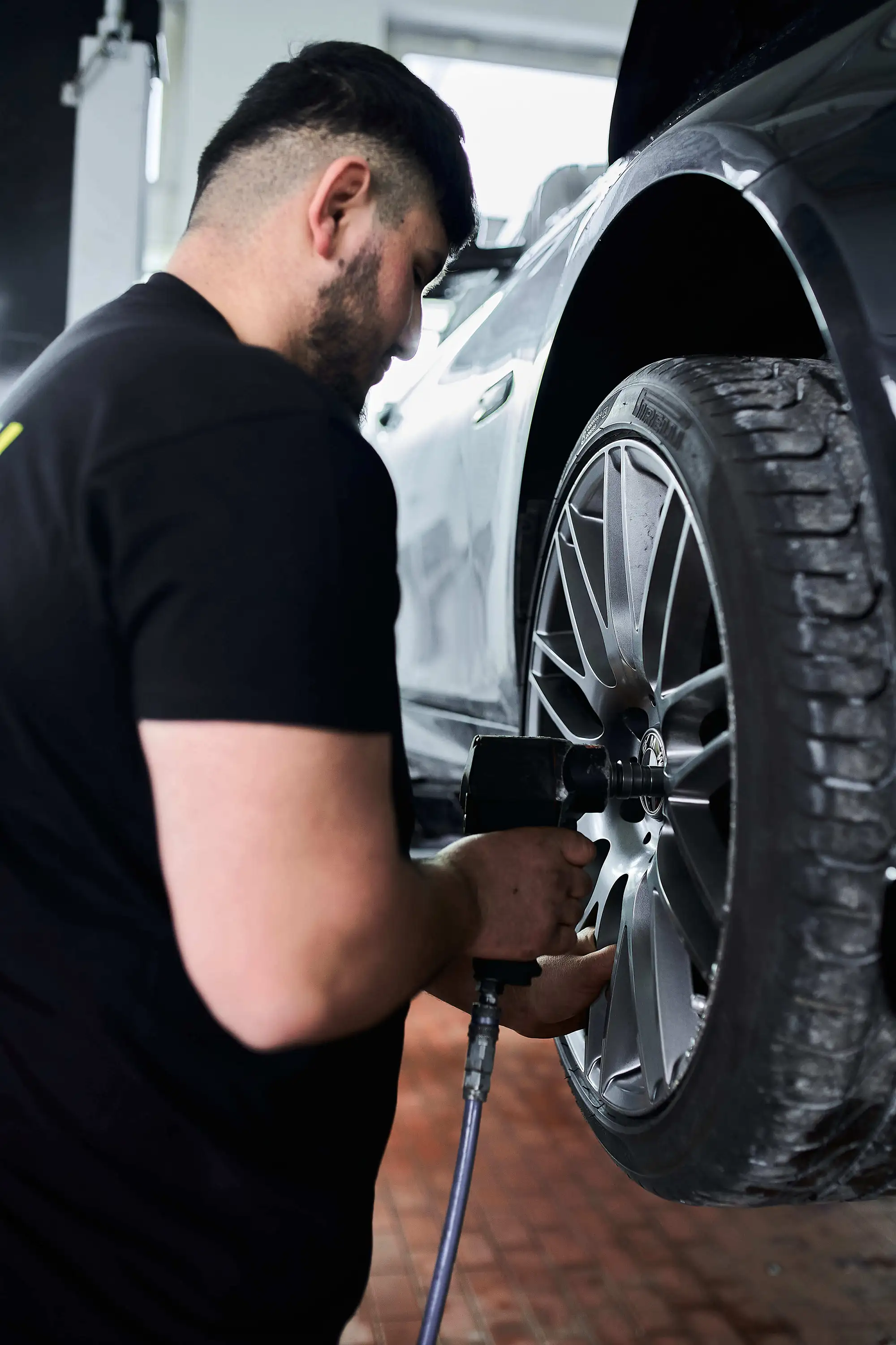 Mechanic using a tool to tighten lug nuts on a car's alloy wheel in a garage.