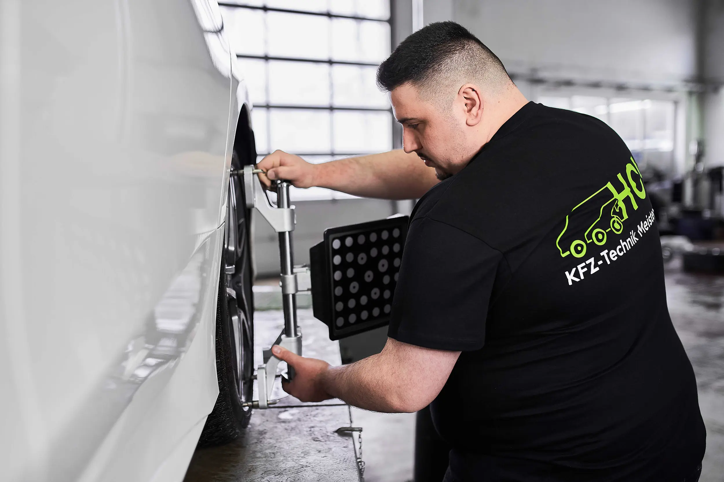 Mechanic adjusting a tool on a car wheel in a garage with bright windows.