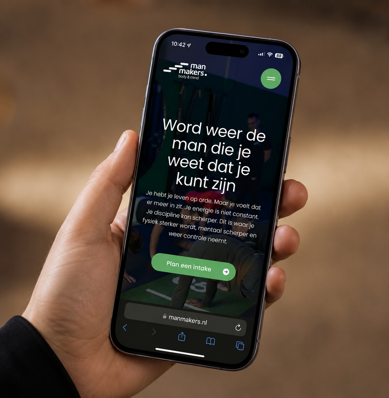 Hand houdt smartphone met Man Makers website voor mannen over fysieke en mentale kracht.