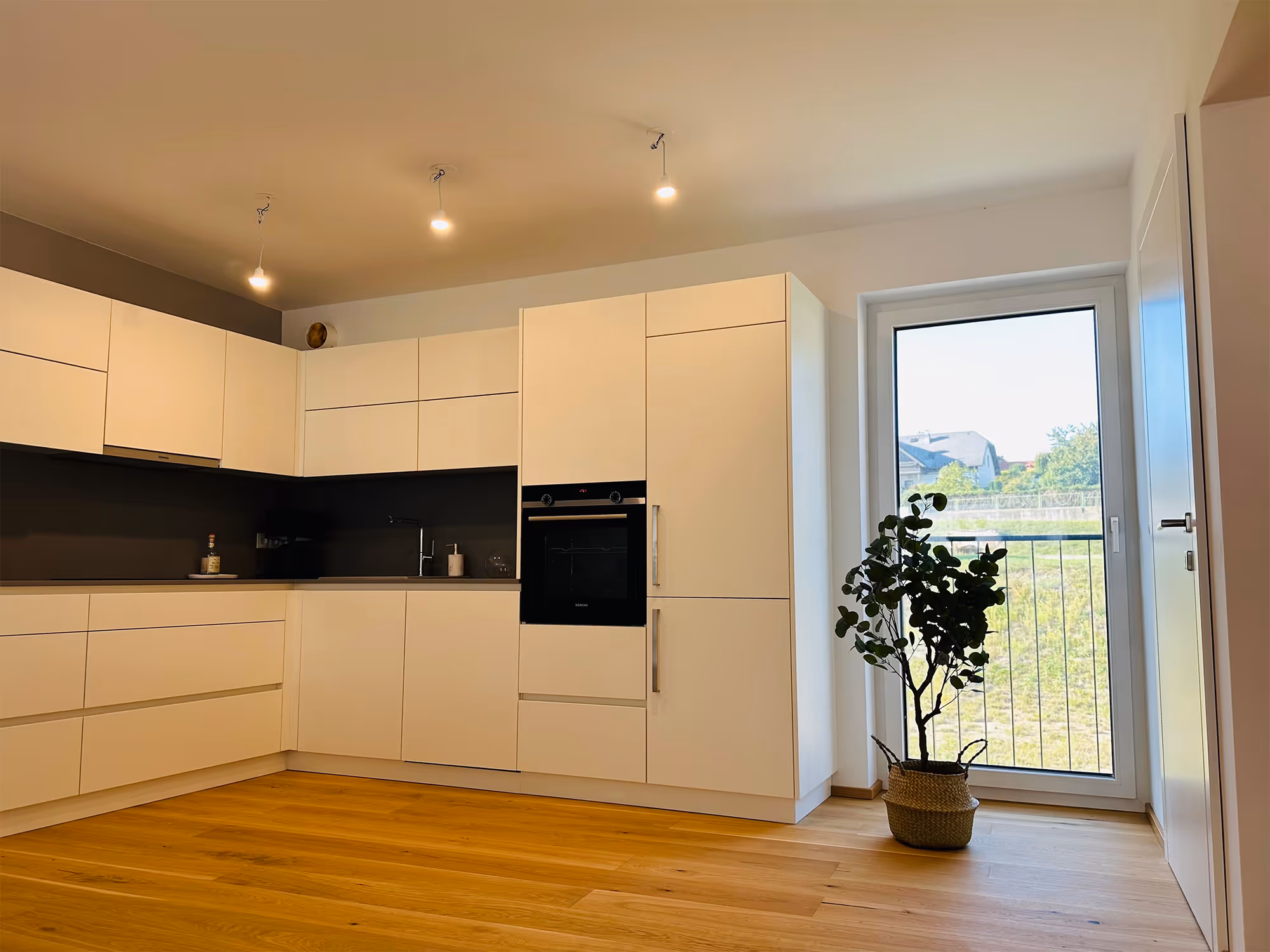 Foto: Moderne weiße Küche mit eingebautem Ofen und Blick in den Garten