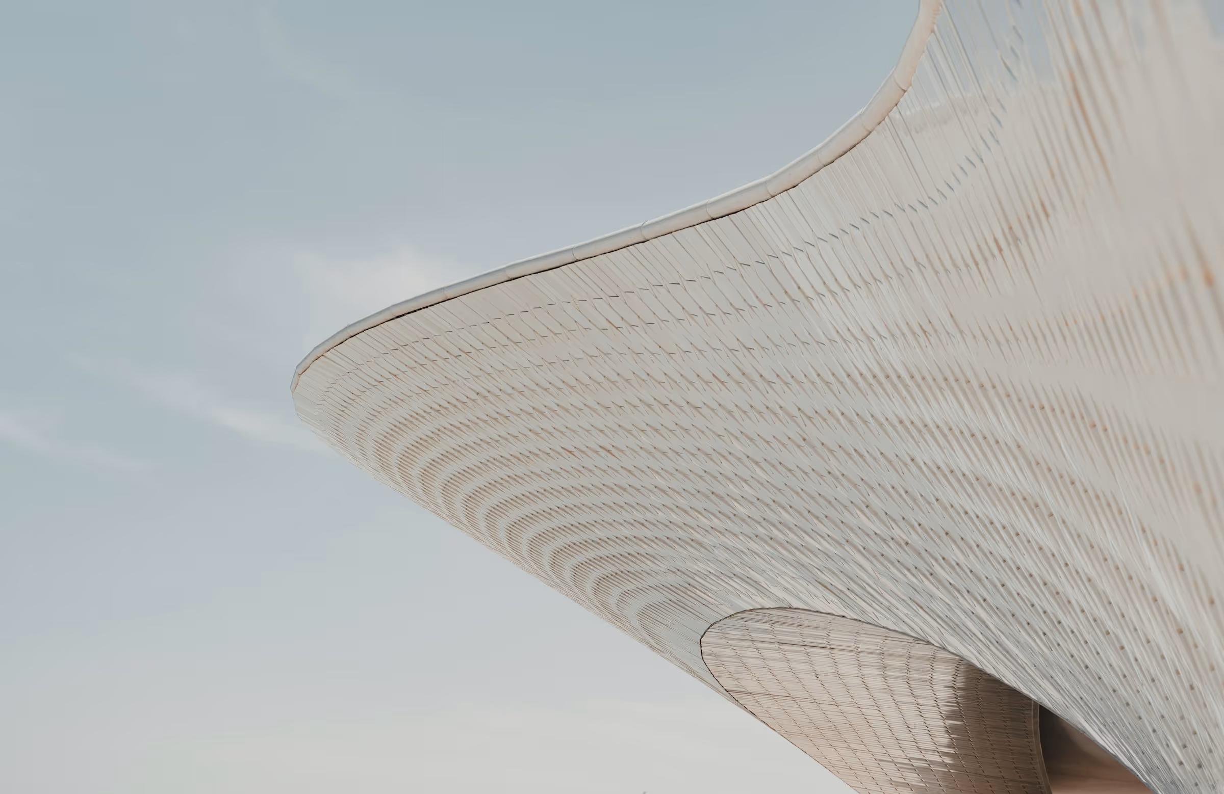 Curved architectural structure with a repeating geometric pattern against a clear sky.