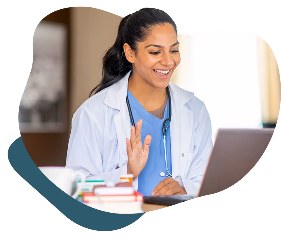 Smiling female doctor in white coat waving during a video call on a laptop.