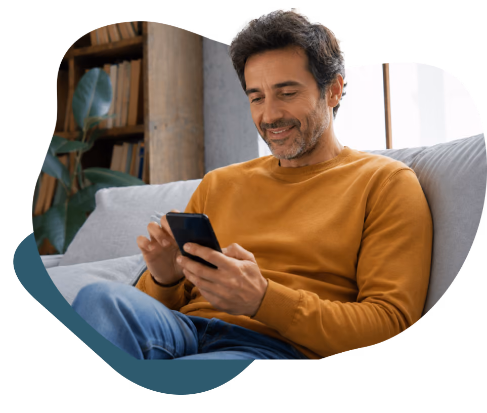 Man wearing glasses sitting at a table, drinking water and looking at his smartphone.