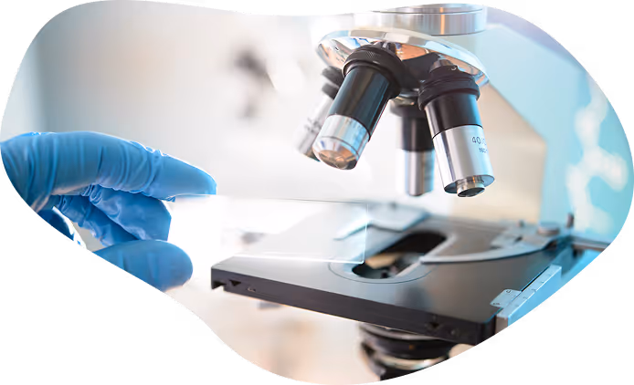 Gloved hand placing a glass slide on a microscope stage in a laboratory setting.