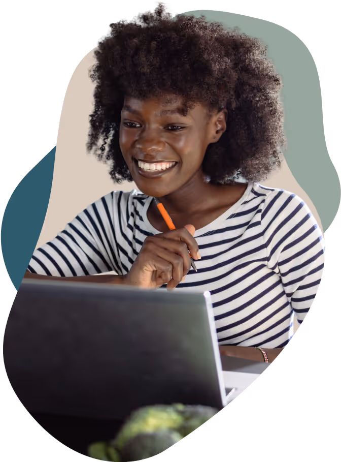 Smiling woman with curly hair in striped shirt working on a laptop while holding a pencil.