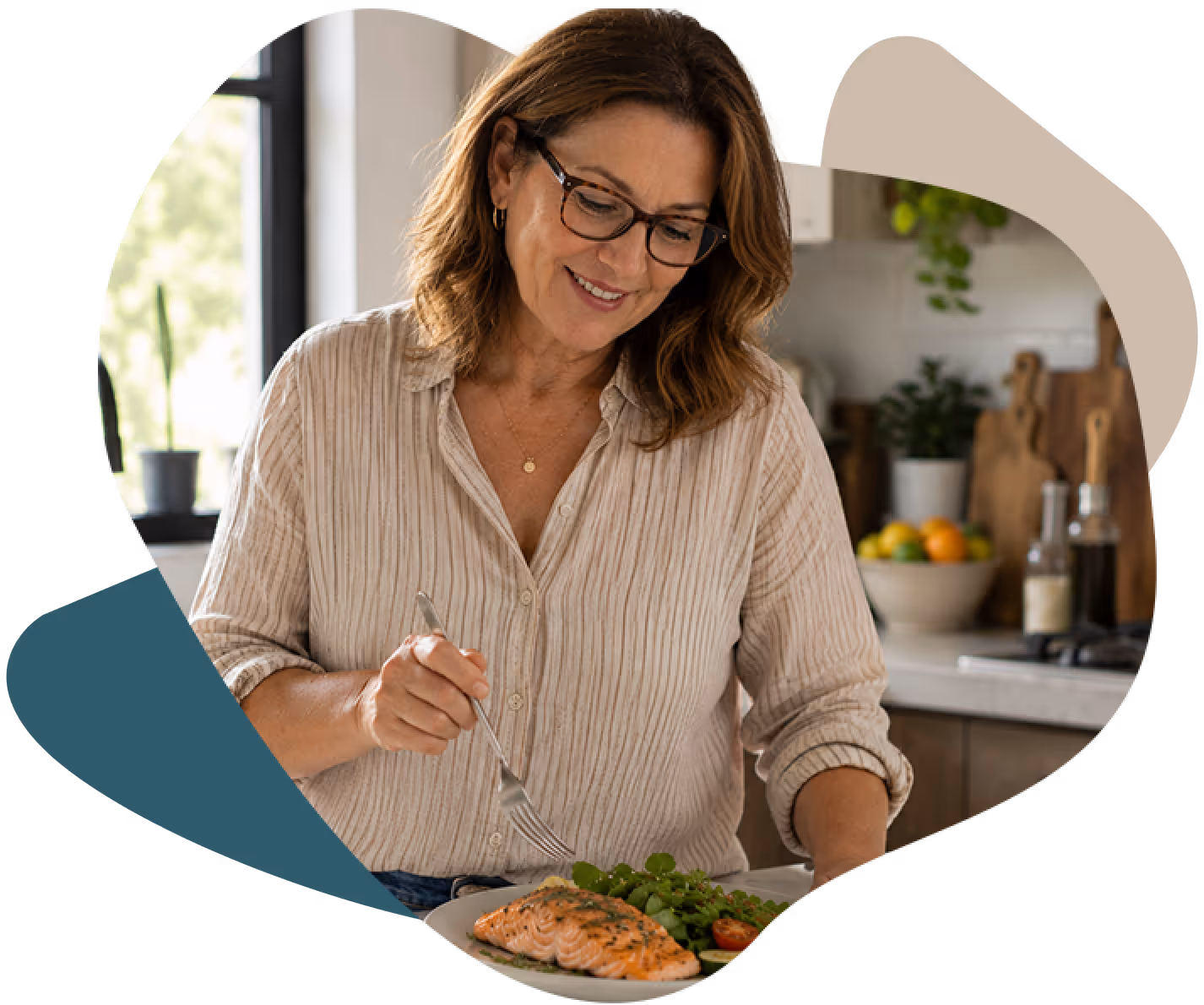 Smiling woman with glasses eating a salmon fillet salad at a kitchen table.