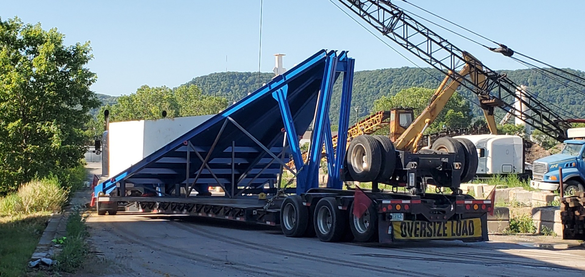 Blue steel structure on a multi-axle trailer marked oversize load
