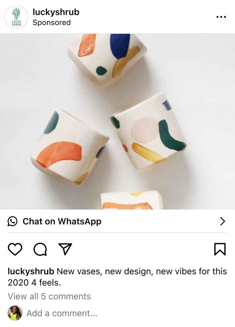 Four white ceramic vases with abstract colorful brushstroke designs in orange, blue, green, and yellow on a white surface.
