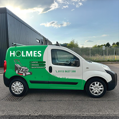 White and green Holmes Garden Care van with lawn mower graphic and phone number on side.