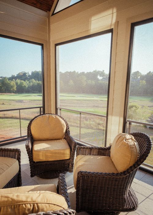 Wicker patio furniture in a screened porch overlooking a golf course