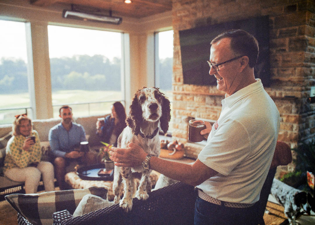 Man playing with his dog in a screened porch while family looks on