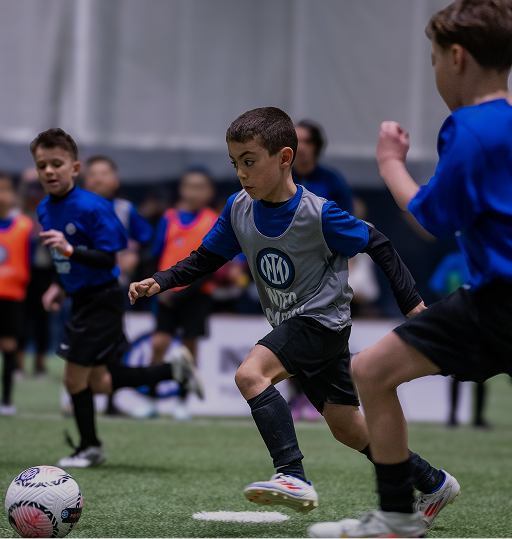 Young boys playing indoor soccer, with one boy in a gray pinnie about to kick a soccer ball.