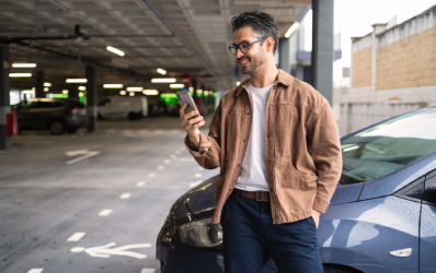 Man checking his phone beside his car in a multi-storey car park
