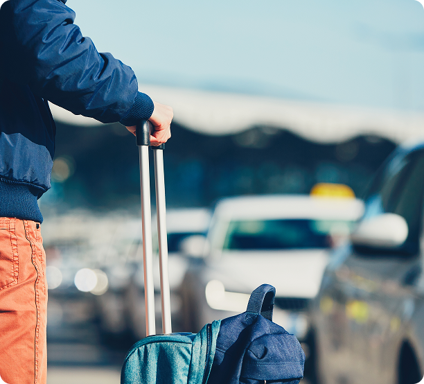 Traveller pulling a suitcase past cars in an airport drop-off area