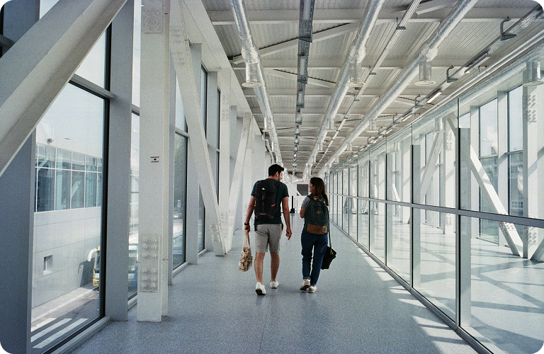 Two travellers walking with bags through a glass airport walkway