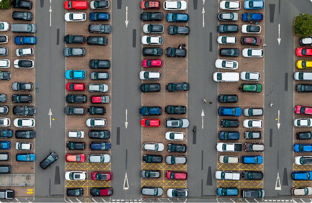 Top-down view of a busy car park with rows of parked cars and one-way lane arrows