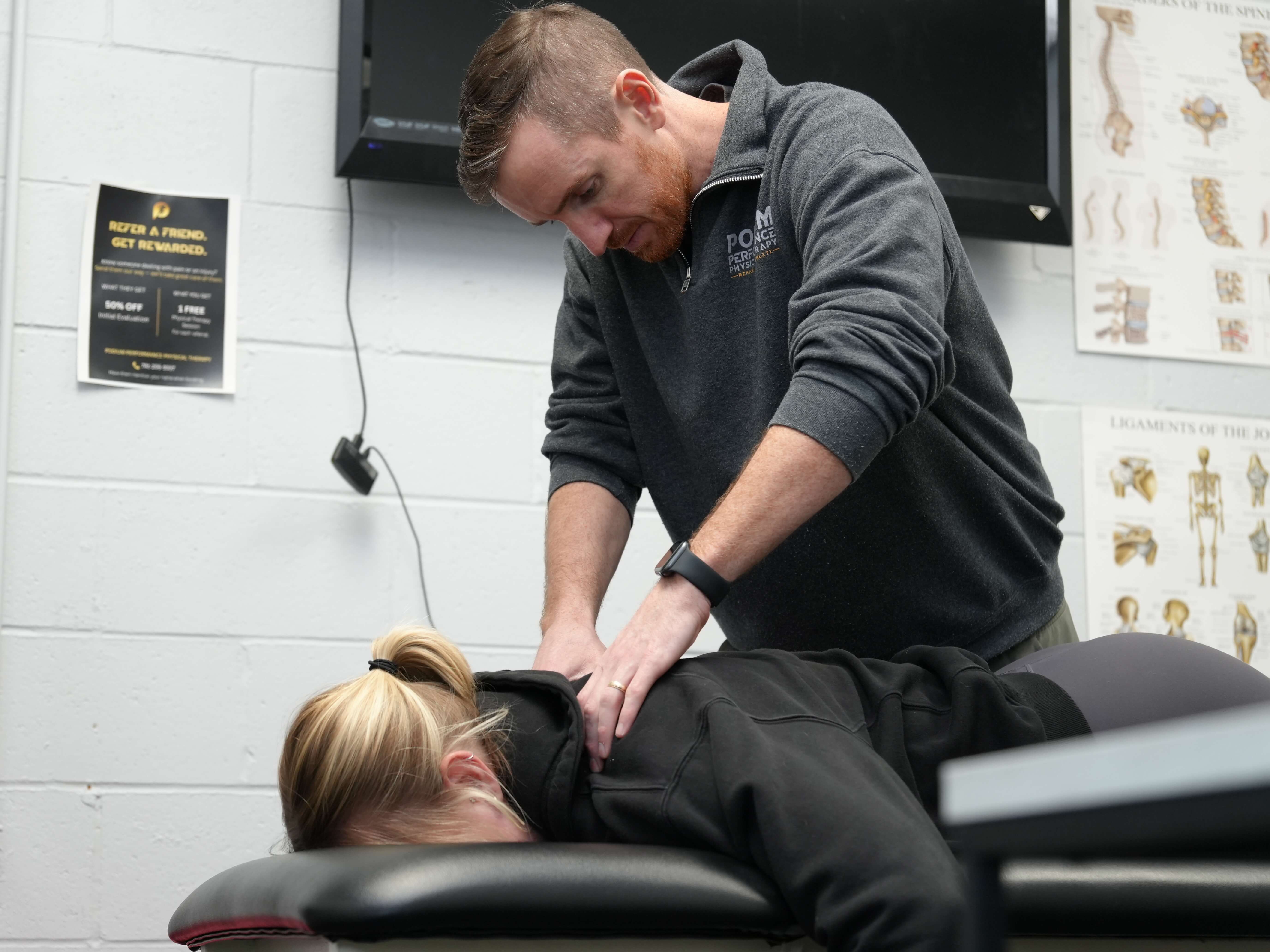 Therapist performing a back adjustment on a woman lying face down on a treatment table in a clinic.