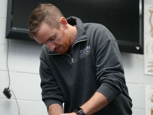 Man in gray zip-up sweatshirt leaning forward, focusing intently on a task.