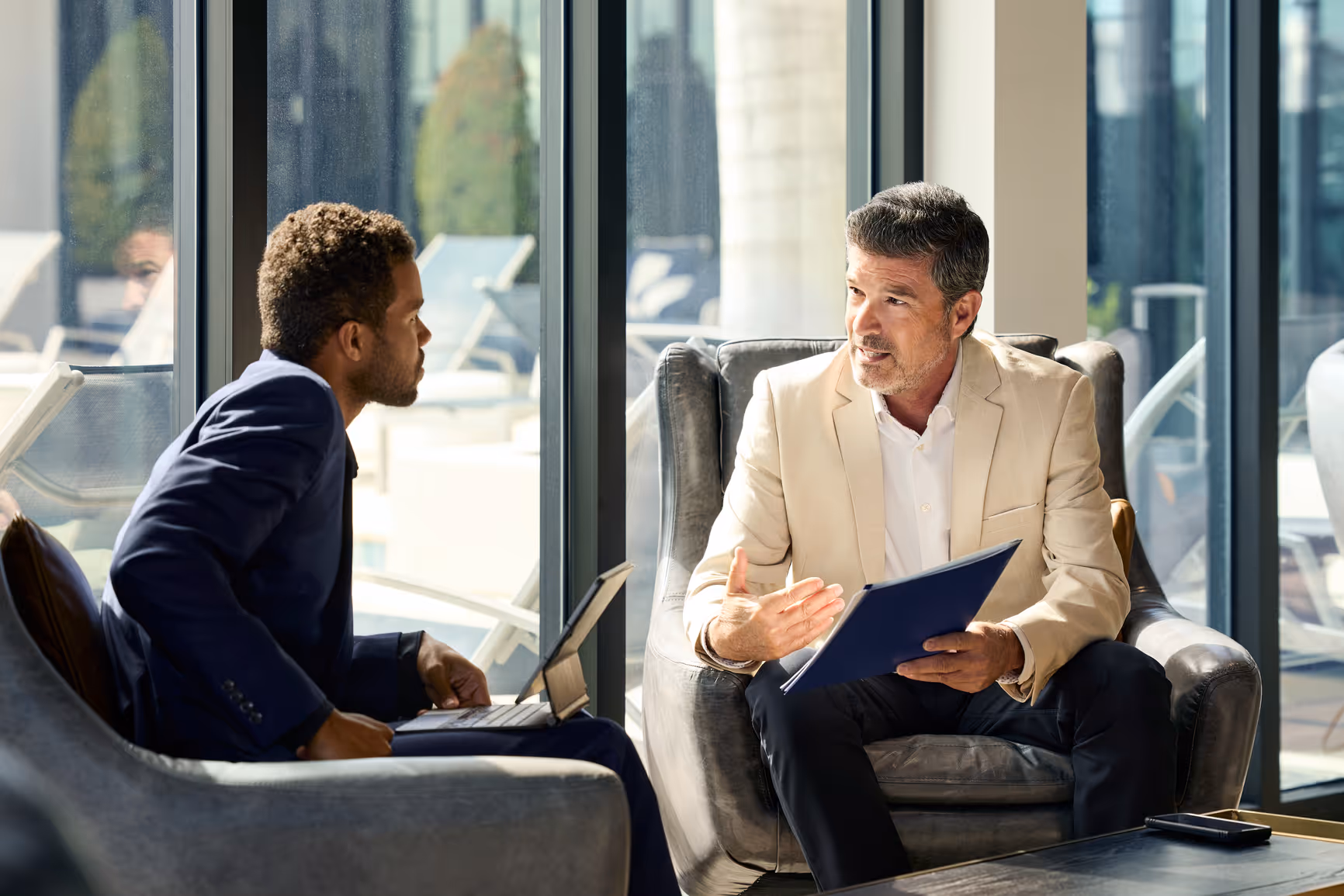 Two business professionals, a woman and a man, walking and smiling in a bright office corridor with large windows.