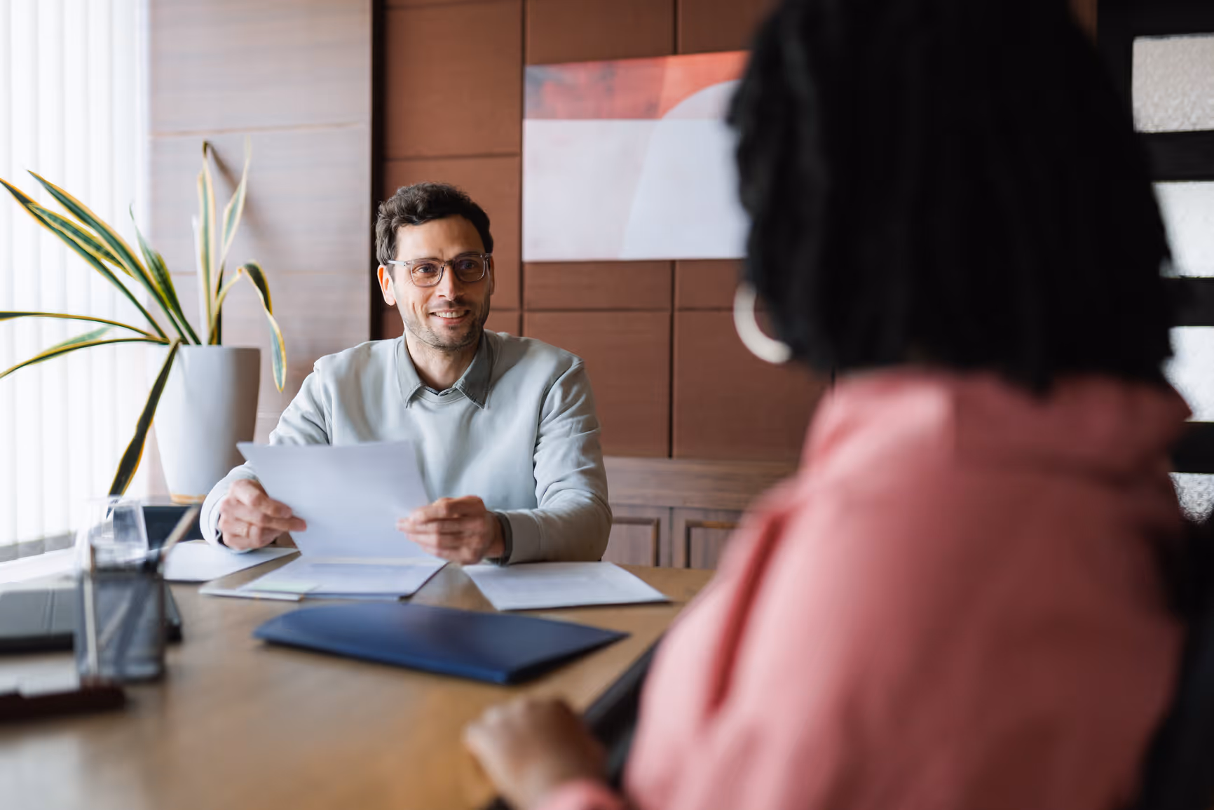 Woman smiling and shaking hands with a man across a desk with papers and a laptop during a meeting.